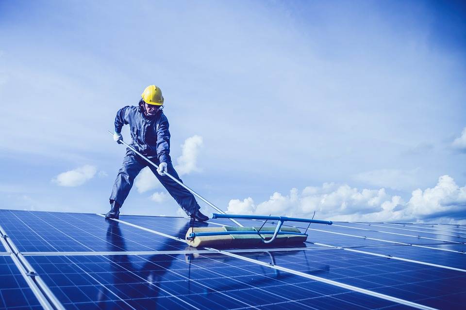 Worker cleaning solar panels equipped with a Micro Inverter against a clear blue sky.