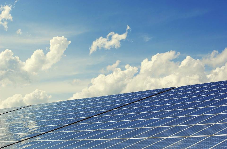 Solar panels with a micro inverter under a cloudy blue sky in the background.