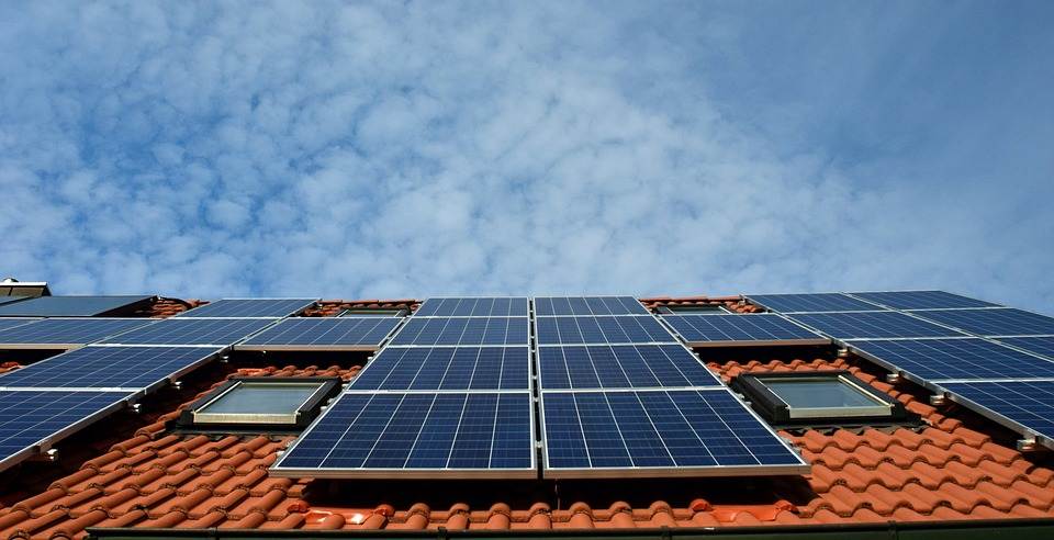 Solar panels with a Micro Inverter installed on the roof of a building against a blue sky with clouds.